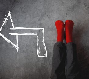 Male legs with red socks leaning on gray wall upside down with drawn direction arrow pointing to left. Youth education youth guidance student guide consultation advisory concept.
